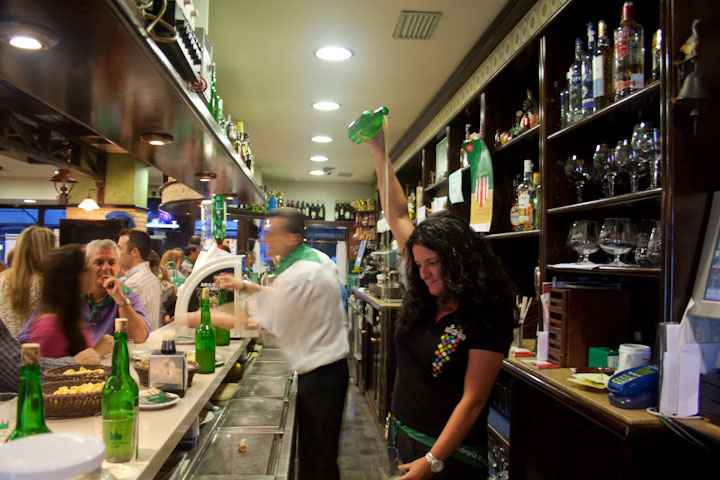 Una mujer escancia sidra asturiana en un bar.